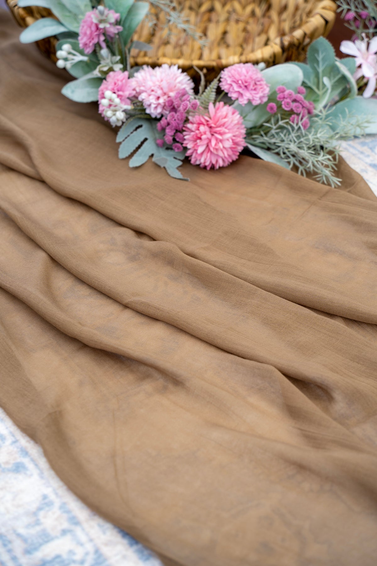 Brown fabric with pink flowers and green leaves on a textured surface