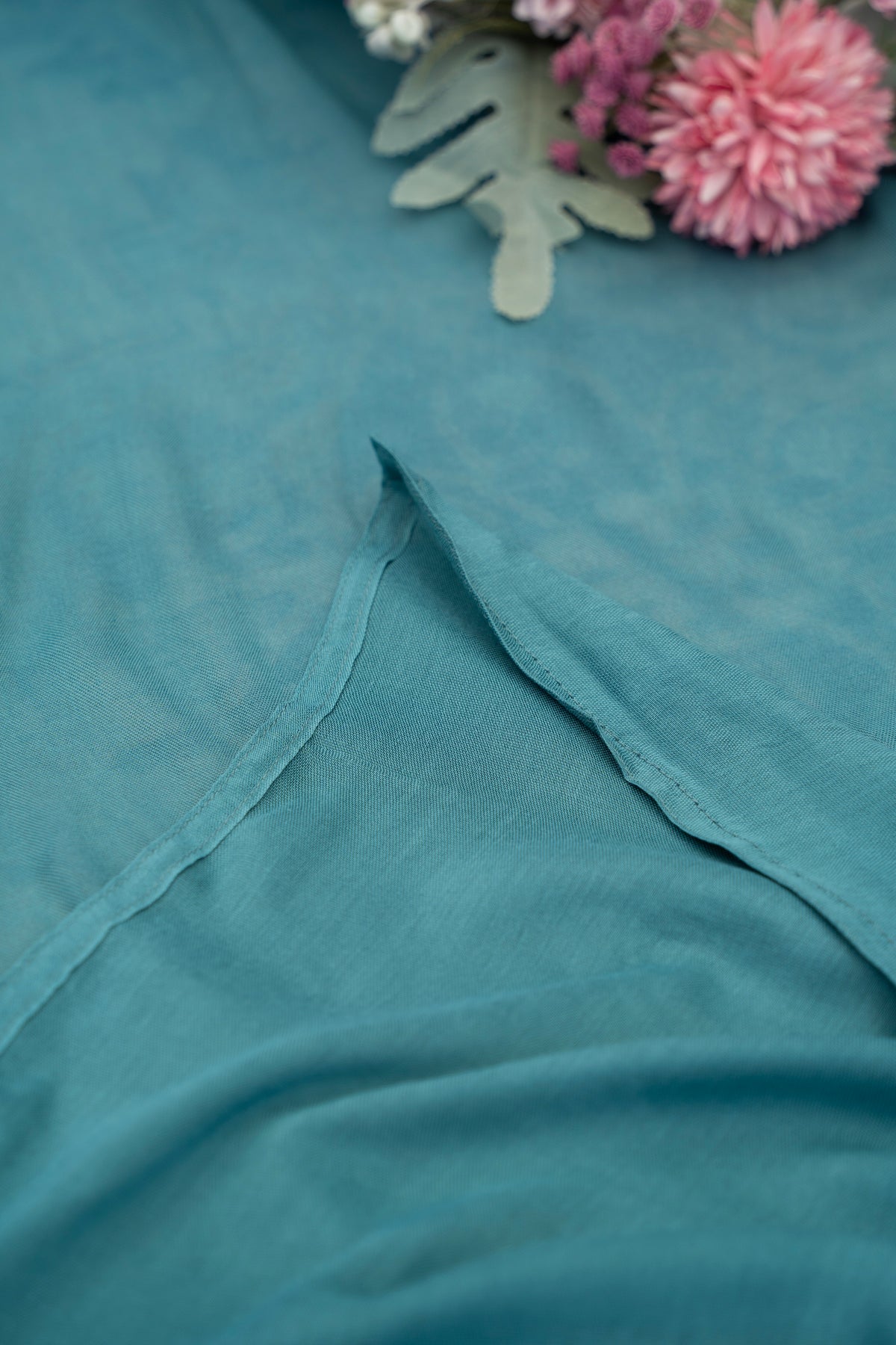 Teal fabric with a close-up of a floral arrangement in the corner.