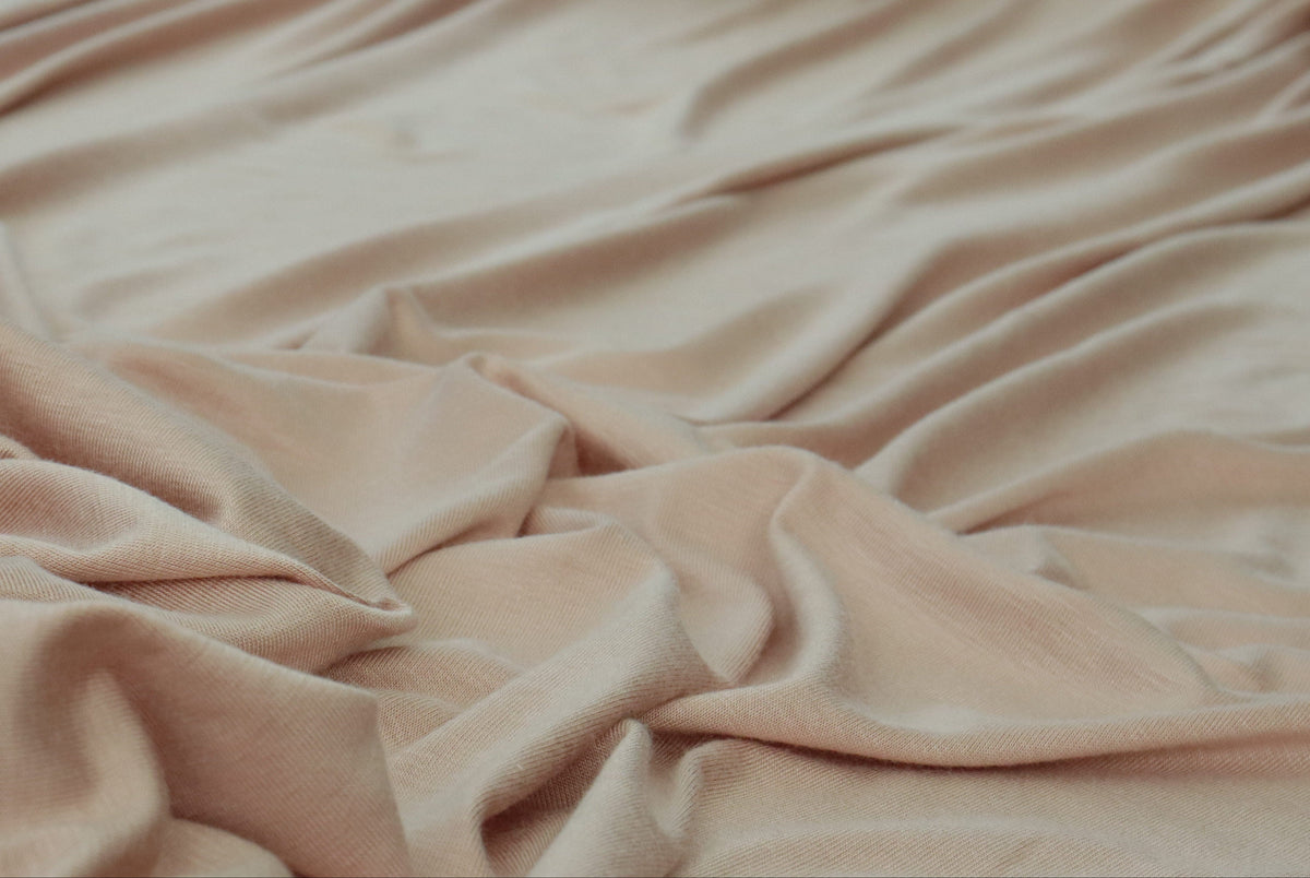A draped piece of soft blush pink fabric with elegant folds and a subtle sheen, styled with decorative flowers in the background.