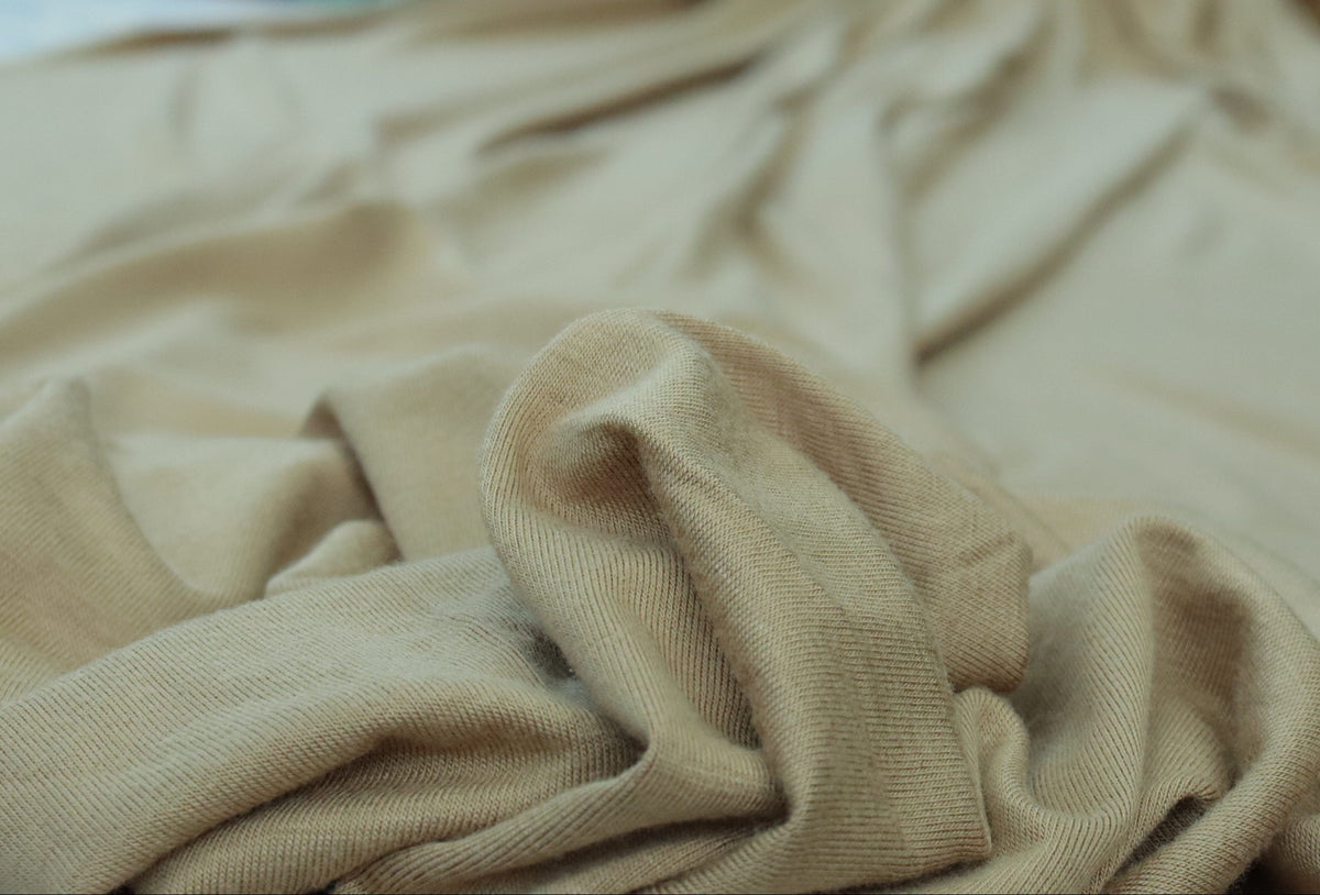 Beige fabric with a blurred background of pink flowers and green leaves.
