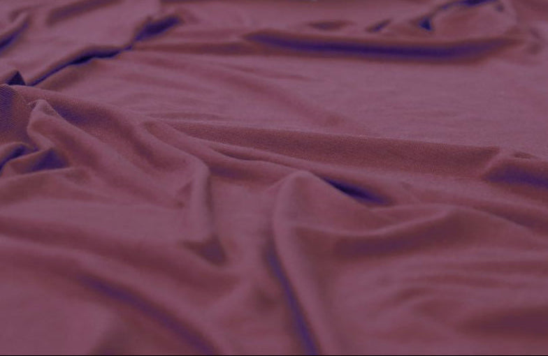 A draped piece of rust-colored fabric, likely a knit sweater or jersey material, spread out on a surface with blurred decorative flowers in the background.