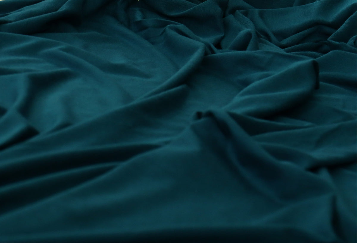 Dark teal green velvet fabric draped in soft folds, with a decorative floral arrangement visible in the upper corner.