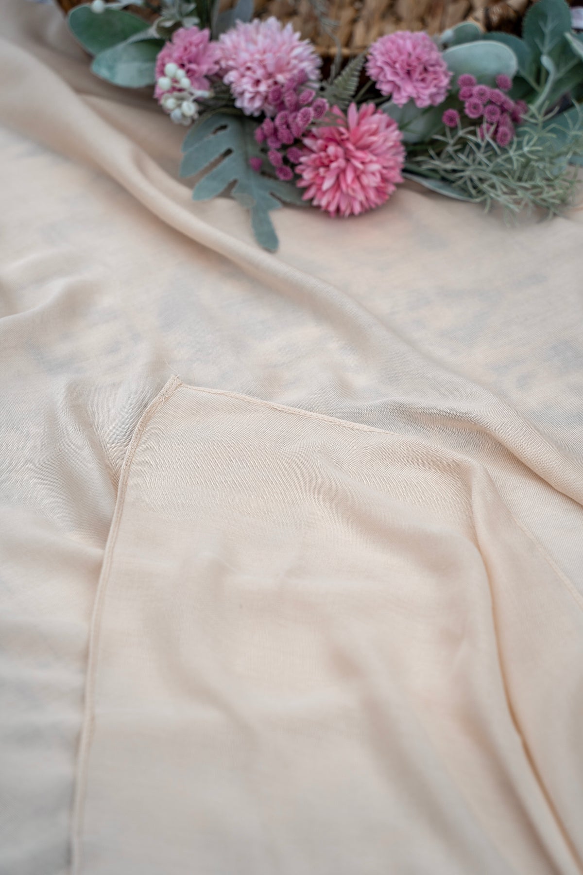 Close-up of a beige fabric with pink flowers and green leaves on a light background