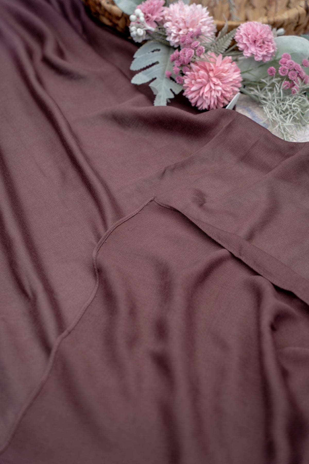 Brown fabric with a basket of pink flowers and greenery in the background