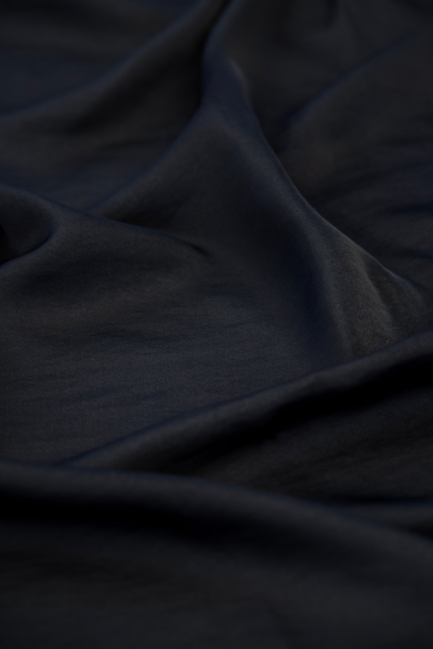 A close-up of draped dark navy fabric with soft folds and a smooth texture.