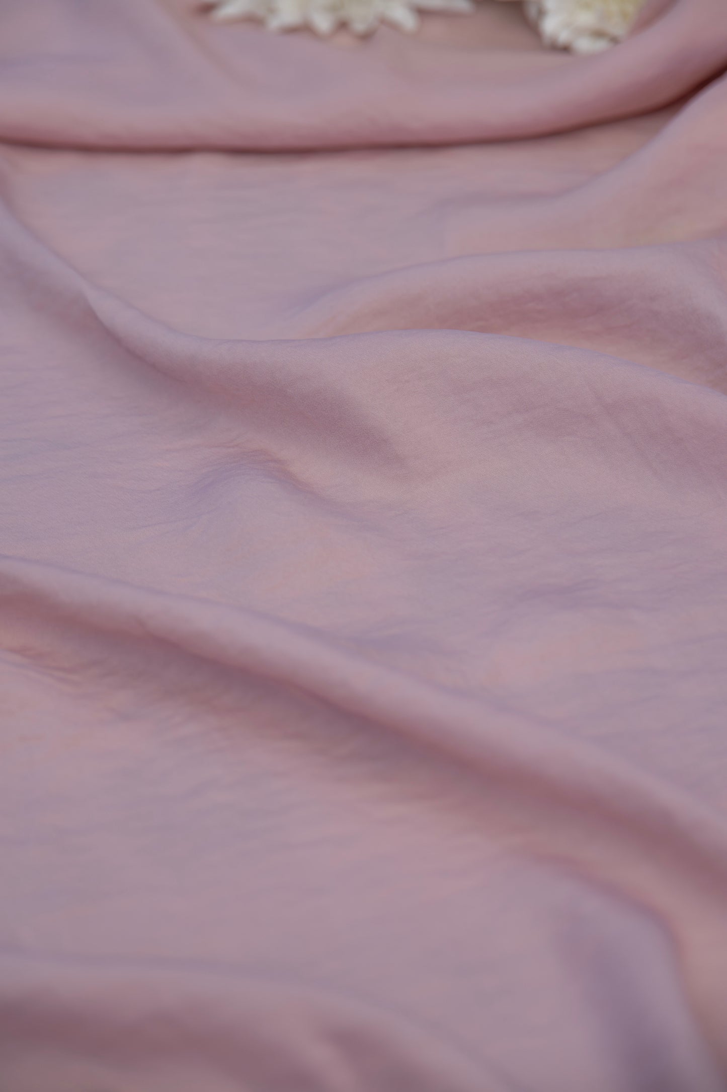 A close-up of draped dusty pink fabric with soft folds and a small white floral detail at the top edge.
