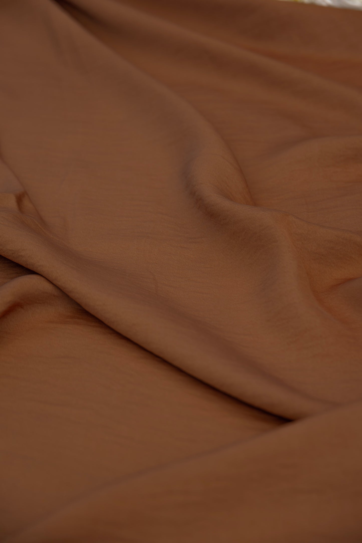 A close-up of draped brown fabric with soft folds and a smooth texture.
