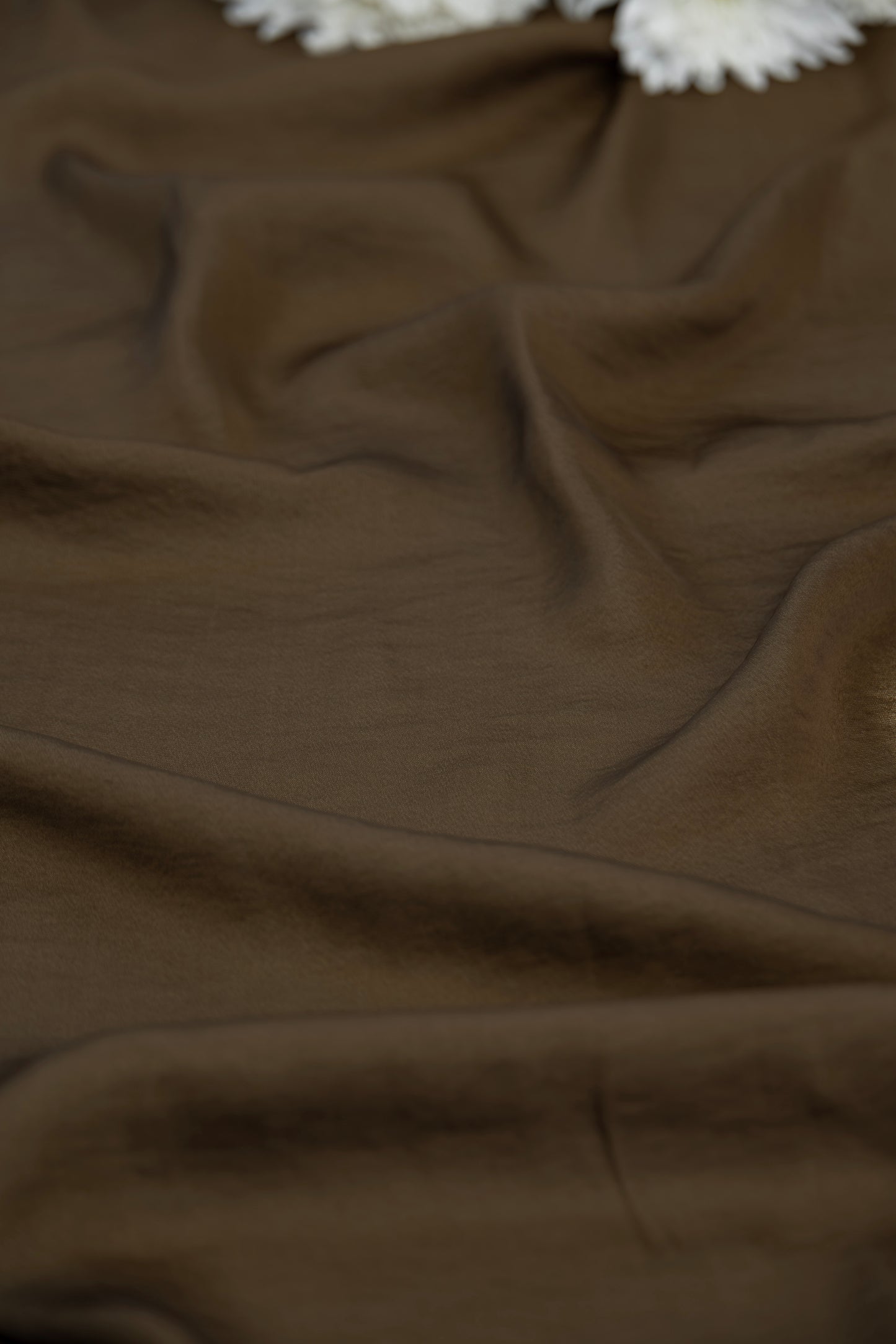 A close-up of draped brown fabric with soft folds and a small white textured accent visible at the top edge.