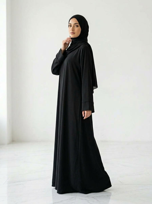 Woman wearing a long, black colour dress and hijab standing in an indoor setting.