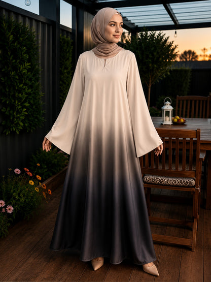 A woman wearing a long-sleeved maxi abaya with a beige-to-dark-gray ombré gradient, paired with a matching hijab, standing on a wooden patio.