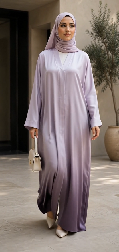 A woman wearing a light lavender to deep purple ombré abaya and matching hijab, walking in a modern outdoor courtyard.