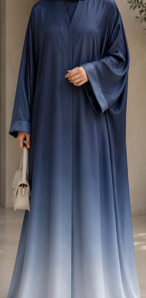 A woman wearing a long flowing abaya in a dark blue to light blue ombré gradient, holding a small light beige handbag.