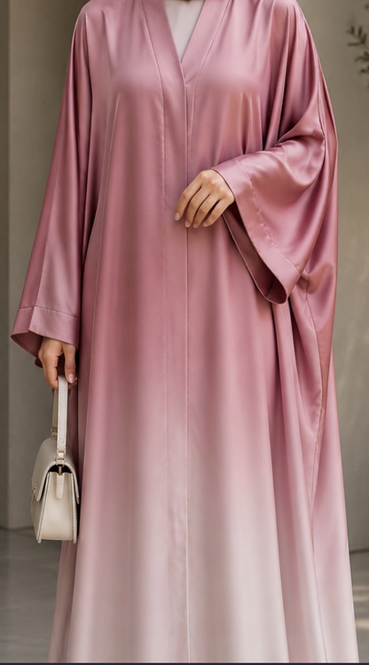 A woman wearing a long, flowing satin-like abaya in dusty pink, holding a small light beige handbag.