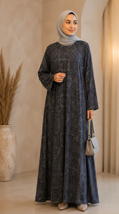A woman wearing a long-sleeved, floor-length dark gray patterned abaya and a light gray hijab, holding a small gray handbag in a warm, neutral-toned indoor setting.