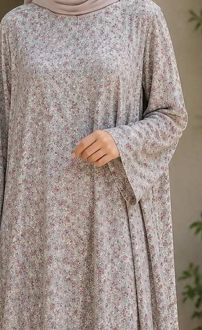 A woman wearing a long-sleeved, loose-fitting abaya dress with a delicate beige and brown floral pattern, paired with a matching hijab.