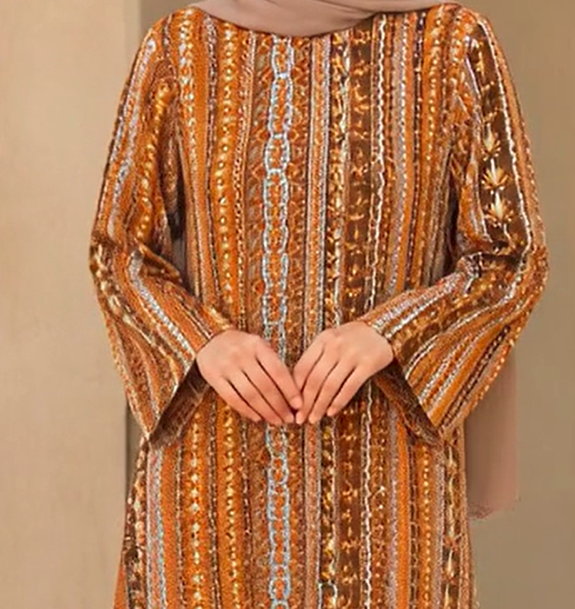 A close-up of a person wearing a long-sleeved, floor-length abaya dress with vertical metallic gold, bronze, and brown embroidered stripes, paired with a beige hijab.