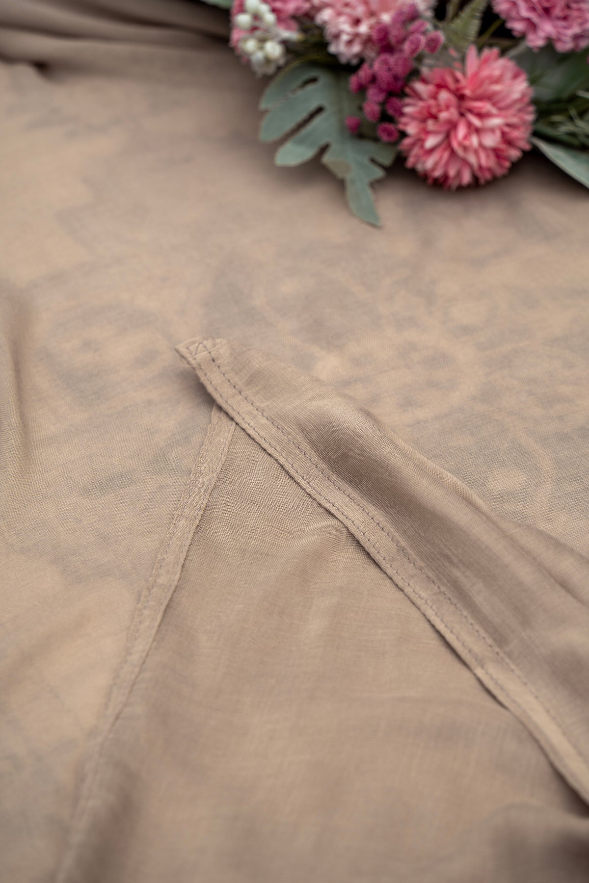 Close-up of beige fabric with lace trim and pink flowers in the background