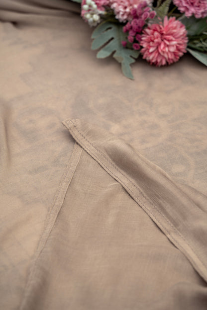 Close-up of beige fabric with lace trim and pink flowers in the background