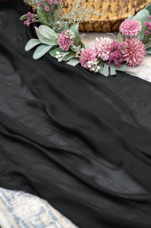 A draped black fabric, likely a silk scarf or sash, styled with pink flowers and green foliage in the top right corner.