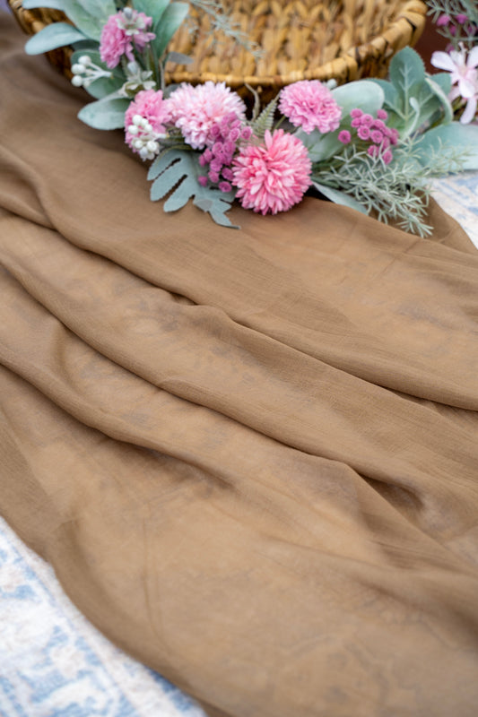 Brown fabric with pink flowers and green leaves on a textured surface