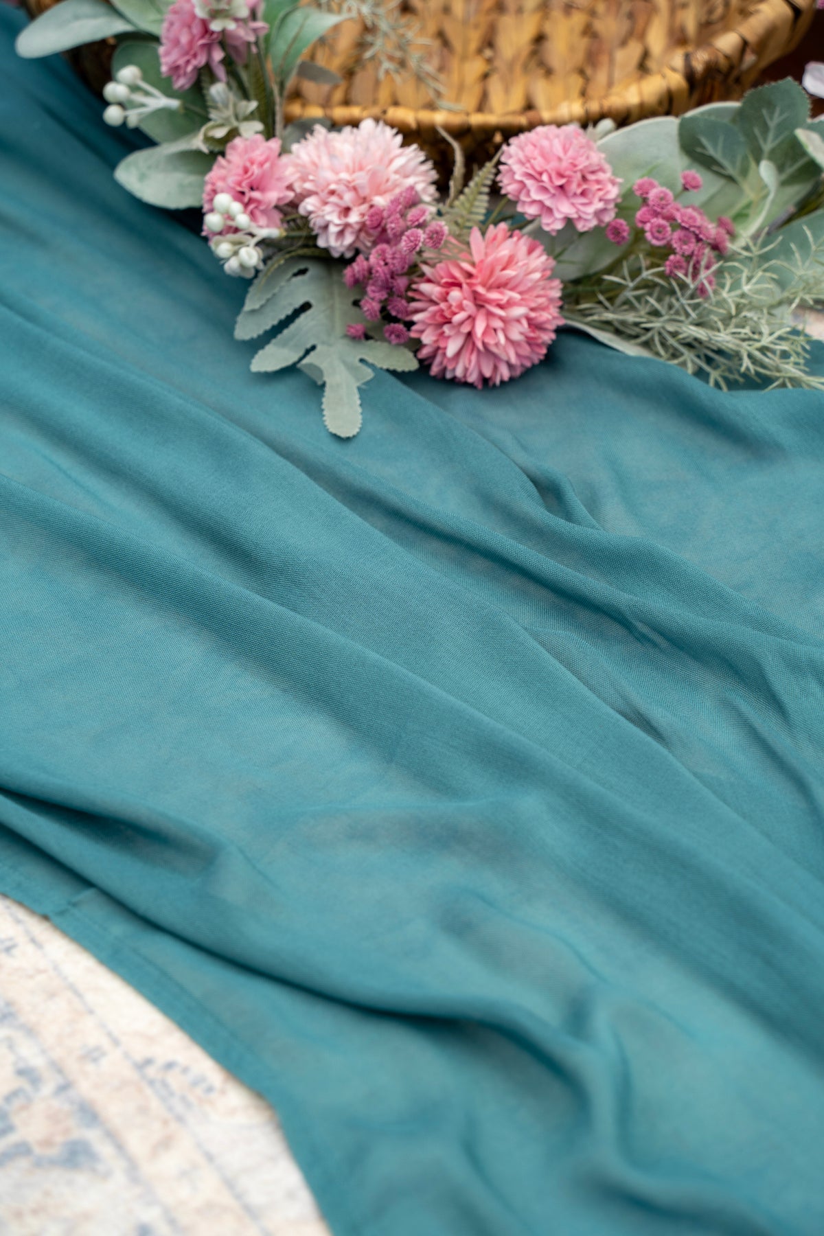 Teal fabric with pink flowers and green leaves on a textured surface