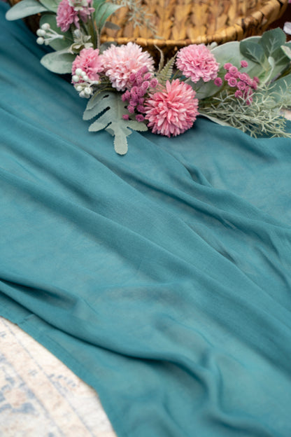 Teal fabric with pink flowers and green leaves on a textured surface