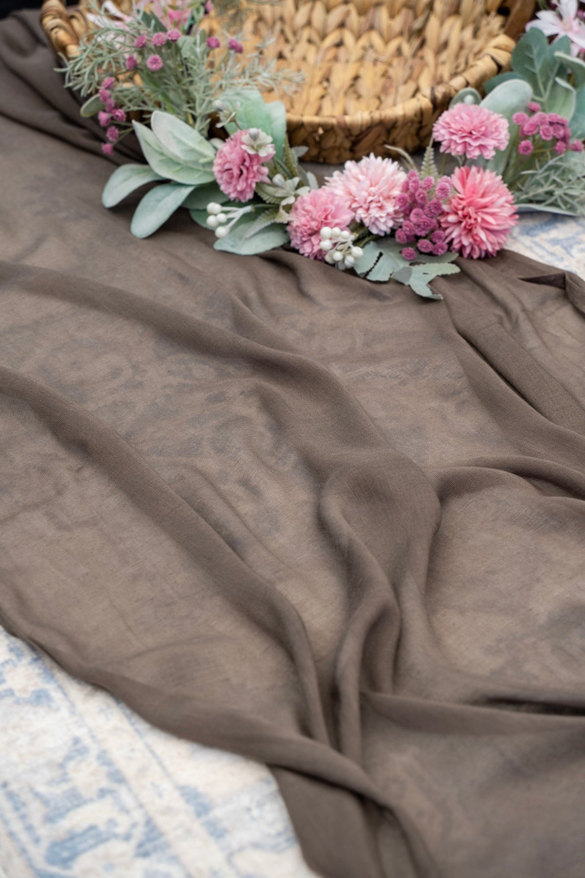 Brown fabric with pink flowers and green leaves on a textured surface
