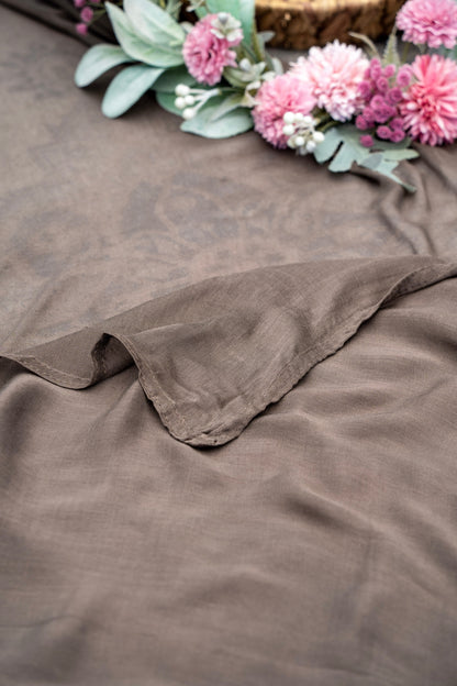 Brown fabric with pink flowers and green leaves on a brown surface