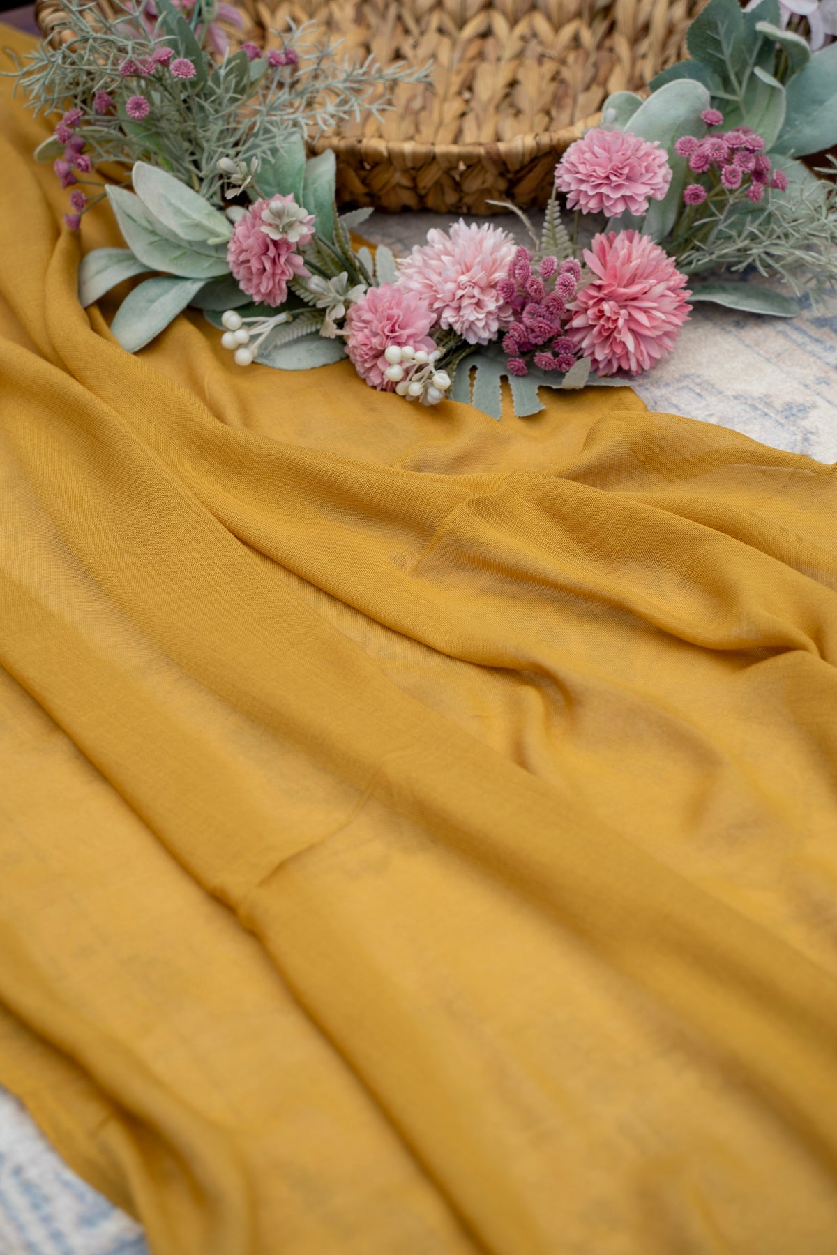 Mustard yellow fabric with pink flowers and green leaves on a textured surface