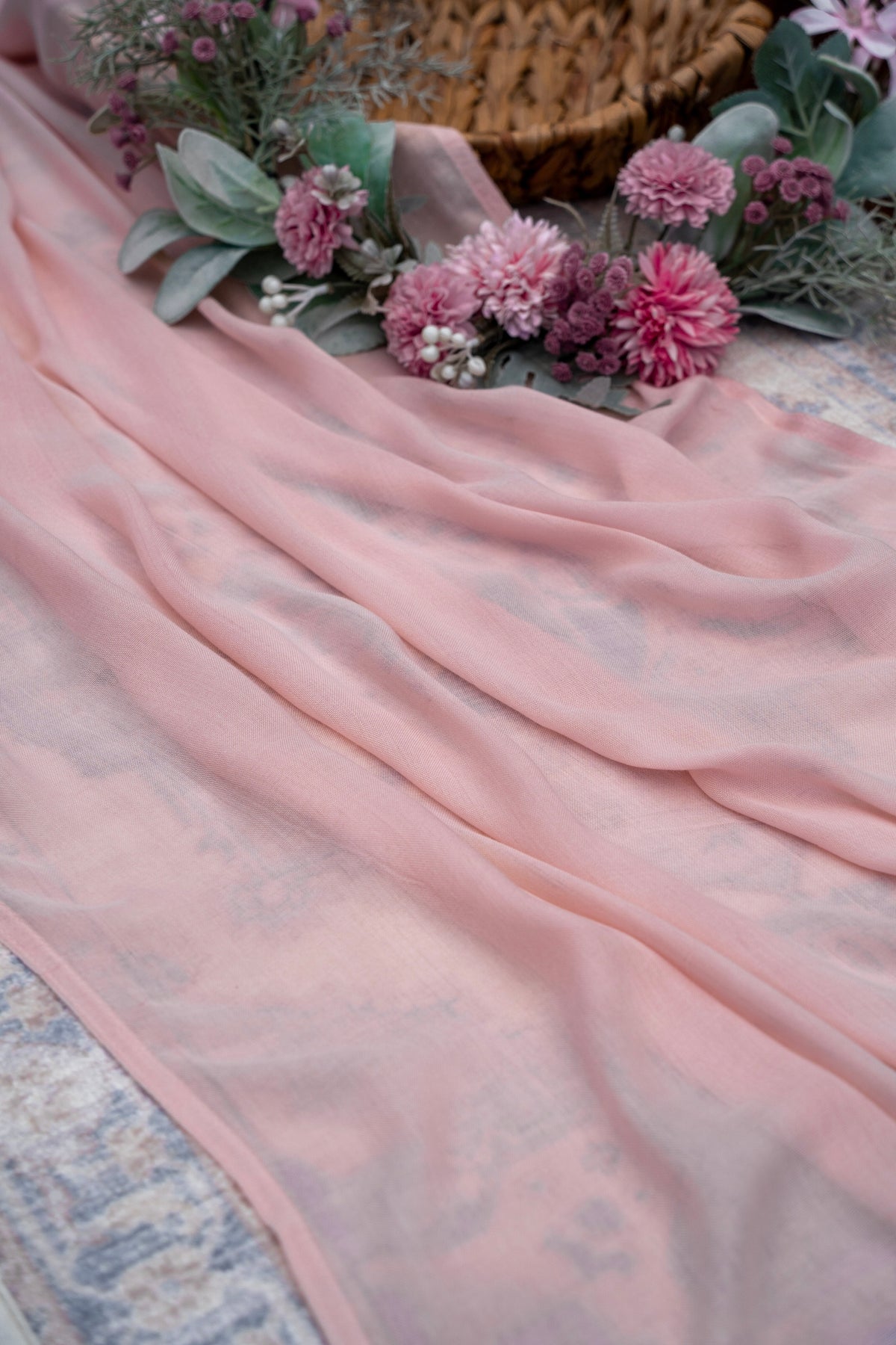 Pink fabric draped over a surface with flowers and greenery in the background