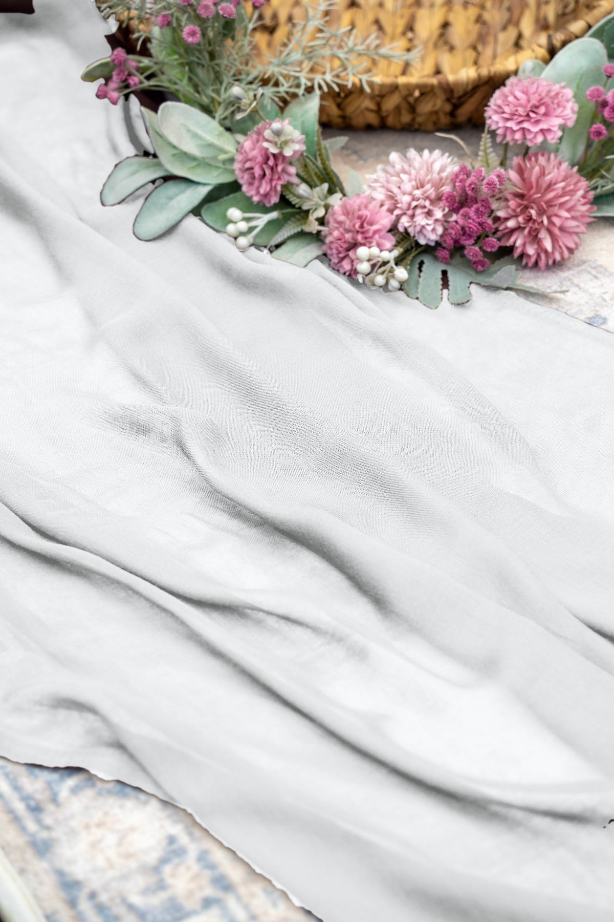 A draped white fabric, likely a silk scarf or sash, styled with pink flowers and green foliage in the top right corner.