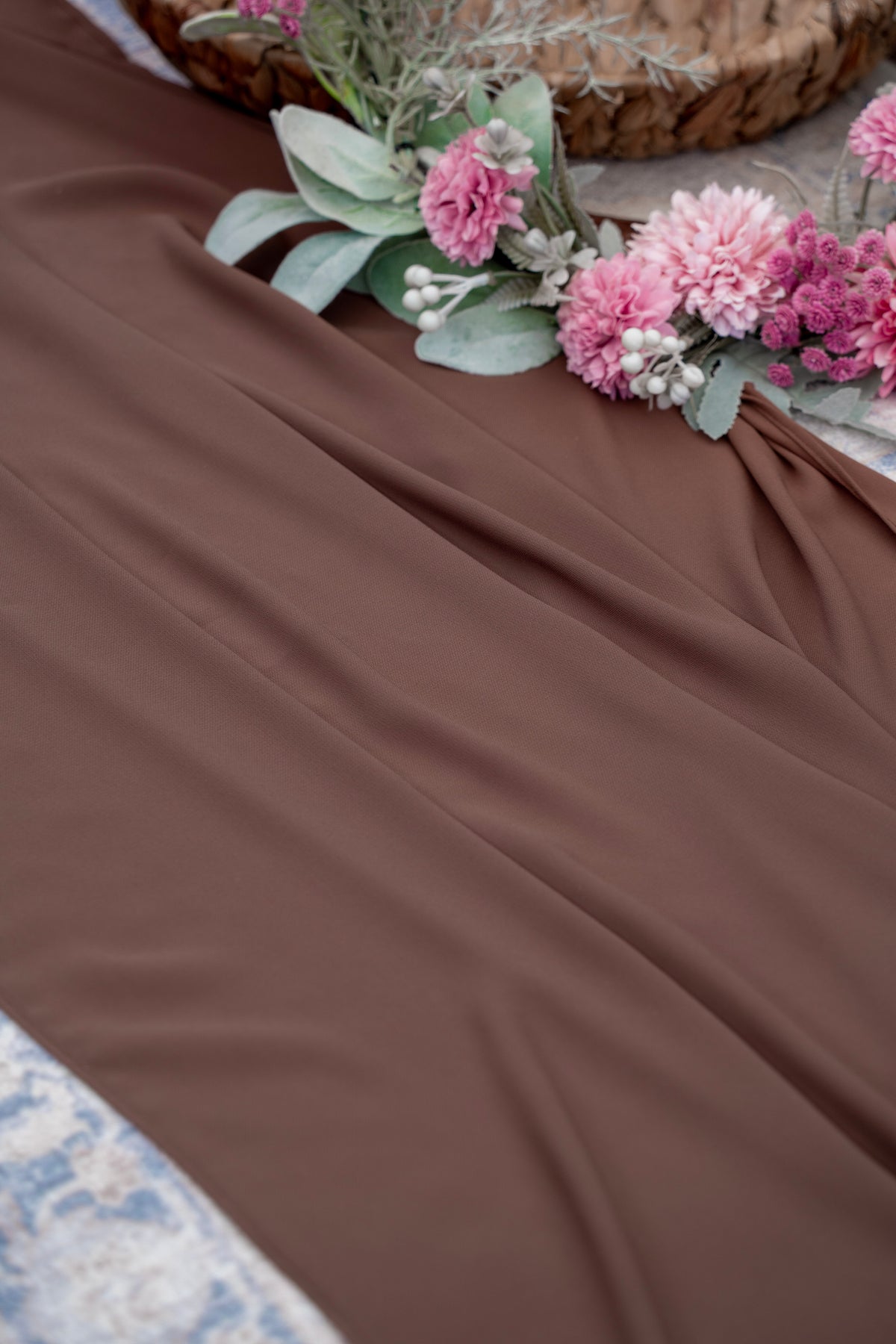 Brown fabric with pink flowers and green leaves on a textured surface