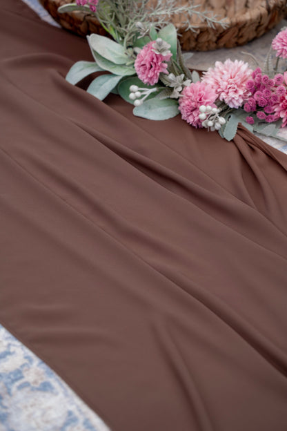 Brown fabric with pink flowers and green leaves on a textured surface