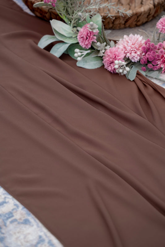 Brown fabric with pink flowers and green leaves on a textured surface