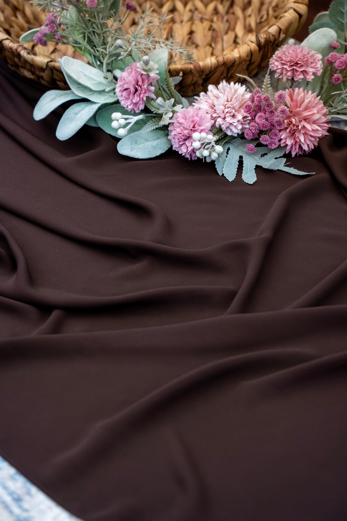 Floral arrangement on a brown fabric surface with a woven basket in the background