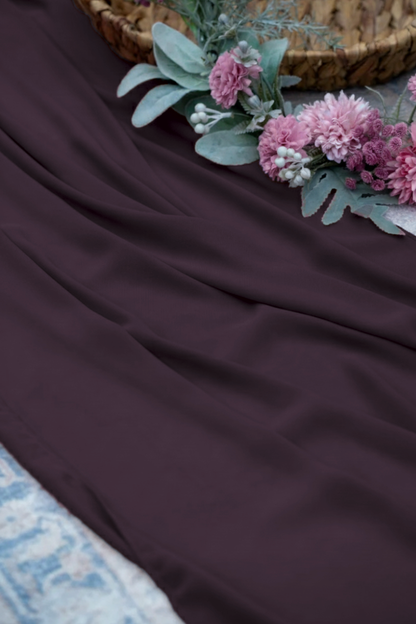 A draped piece of dark plum purple fabric, styled with pink flowers and green leaves in the upper right corner.