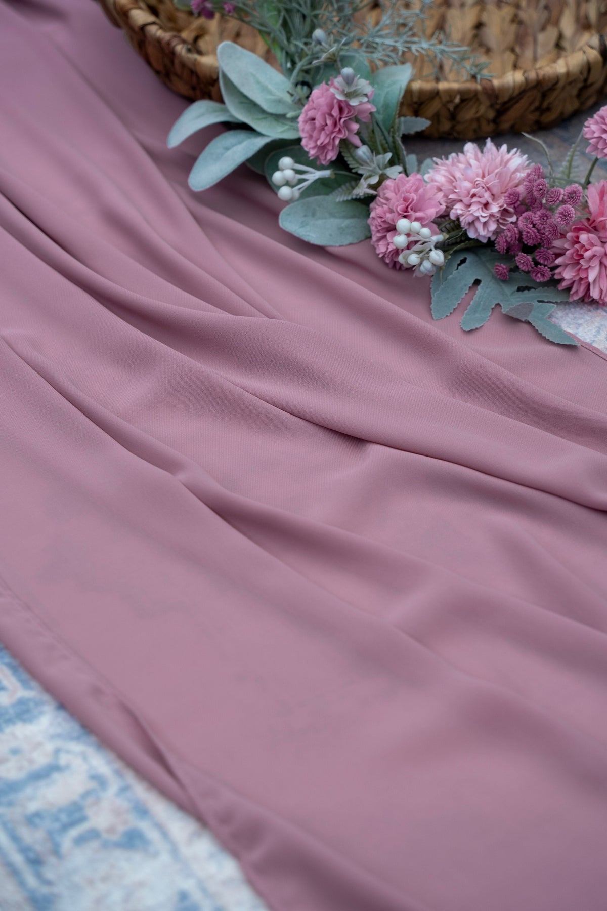 Pink fabric with flowers and a woven basket on a textured surface