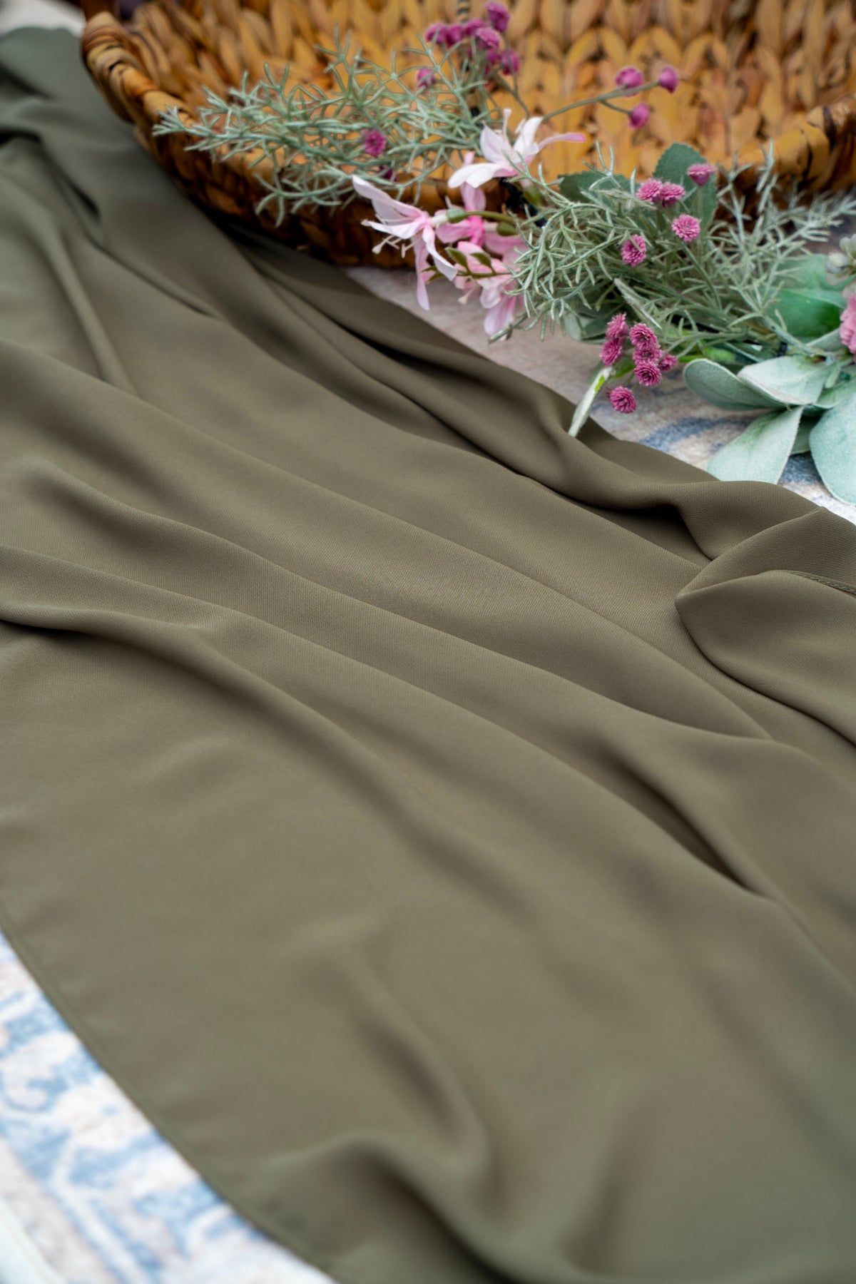 Olive green fabric with a woven basket and flowers in the background