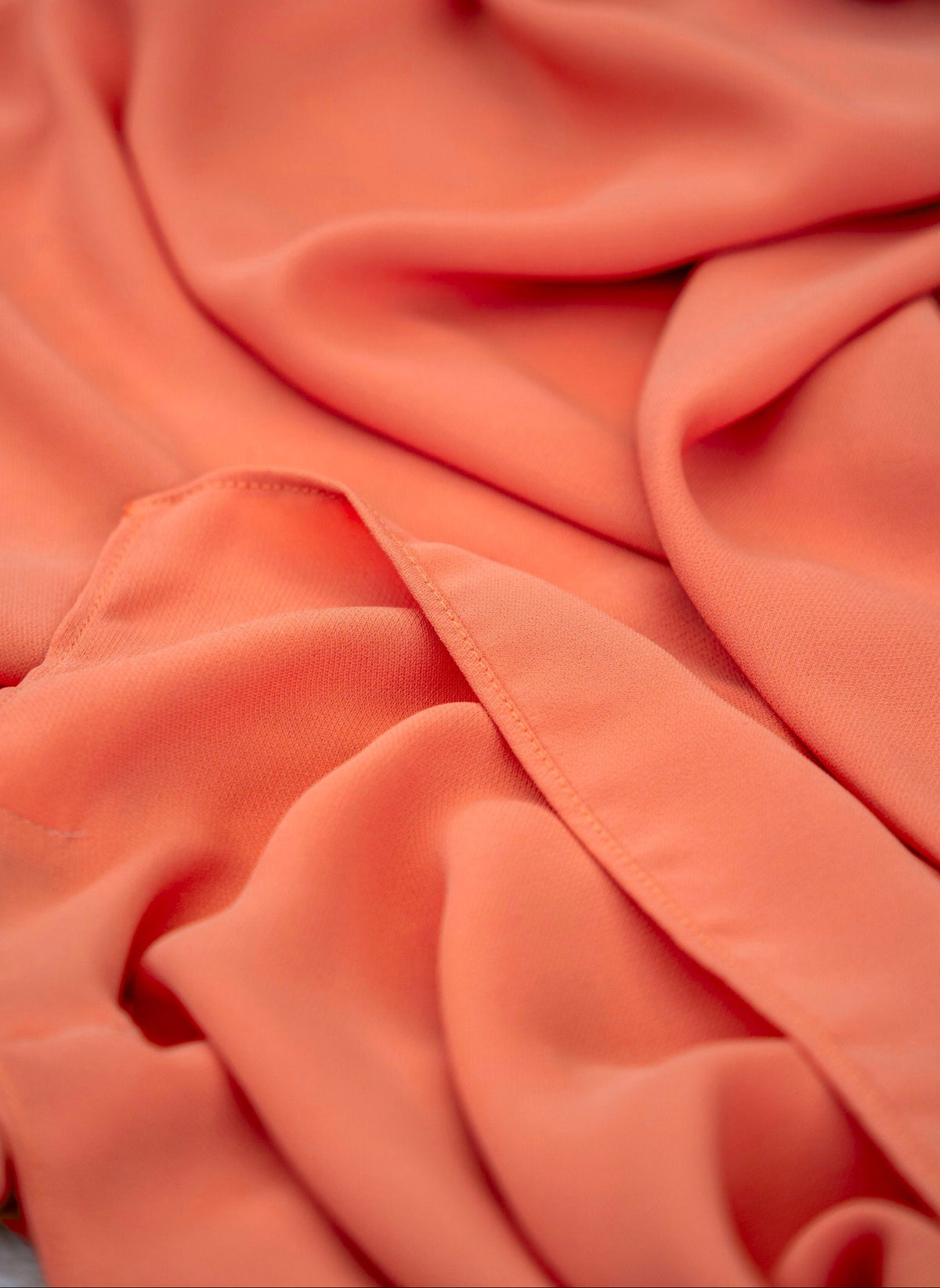 A close-up of draped peach-orange fabric with soft folds and a subtle sheen, filling the frame.
