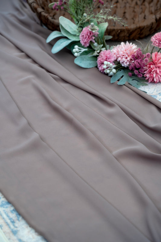 Brown fabric with pink flowers and green leaves on a textured surface