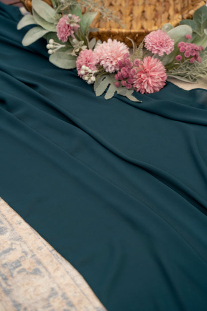 Teal fabric with pink flowers and green leaves on a textured surface
