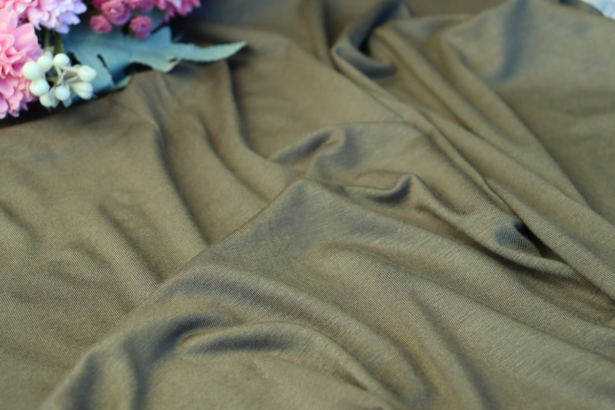 A close-up of draped olive green fabric with soft folds, with a small cluster of pink and white flowers placed in the upper left corner.