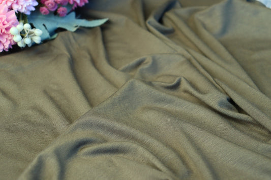 A close-up of draped olive green fabric with soft folds, with a small cluster of pink and white flowers placed in the upper left corner.