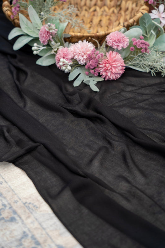 Floral wreath with pink flowers and green leaves on a dark fabric background