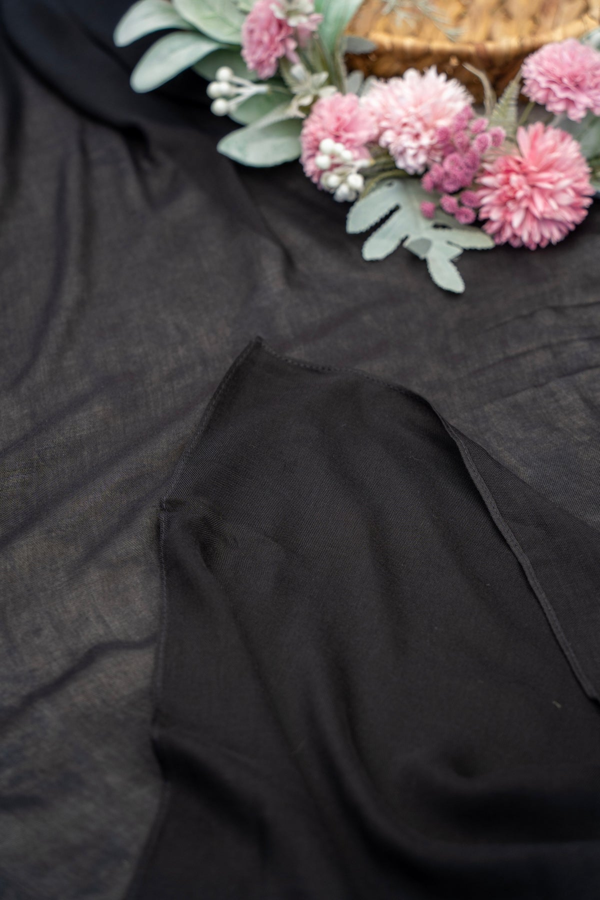 Black fabric with pink flowers and green leaves on a dark background