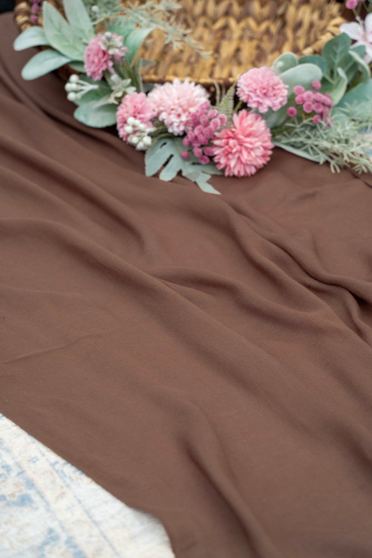Brown fabric with pink flowers and green leaves on a textured surface