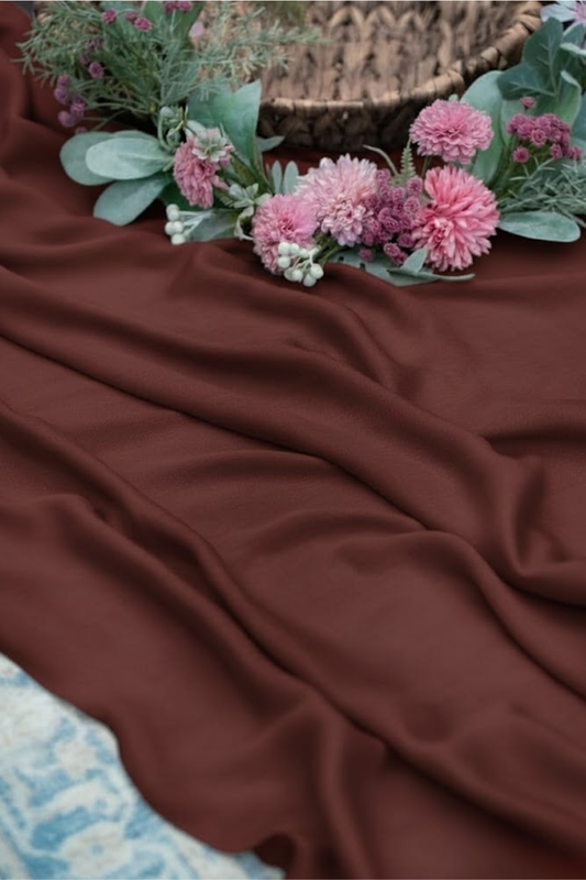 Brown fabric with pink flowers and green leaves on a textured surface