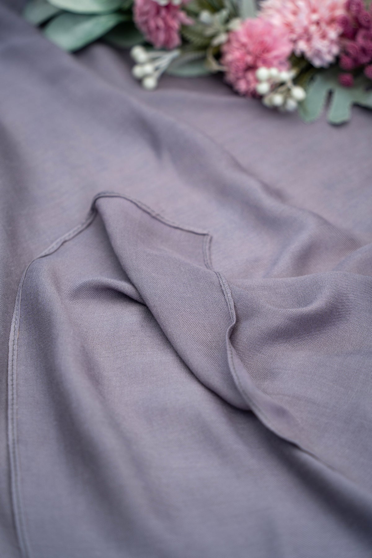 Close-up of gray fabric with a blurred background of pink flowers and green leaves.