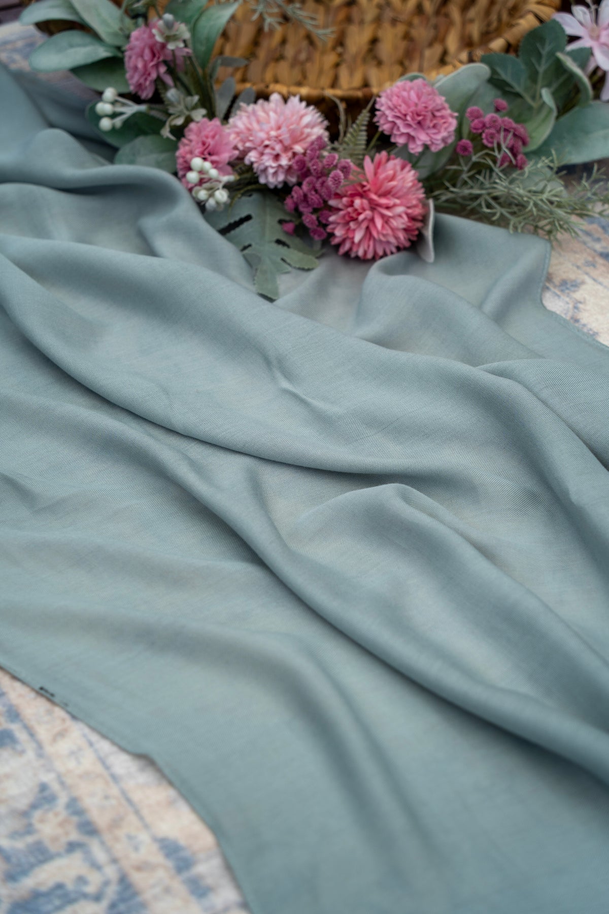 Light blue fabric draped over a surface with pink flowers and greenery.