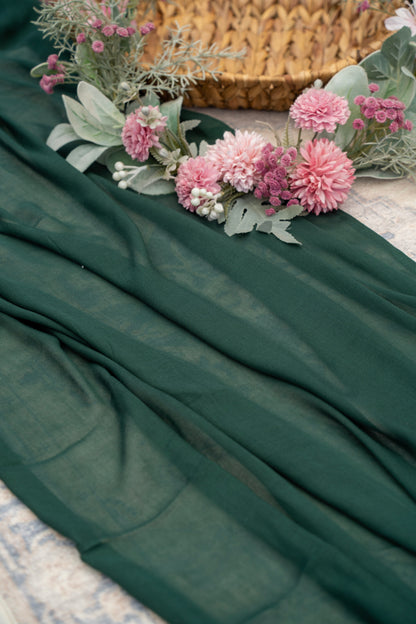 Teal-green fabric with pink flowers and greenery on a textured surface